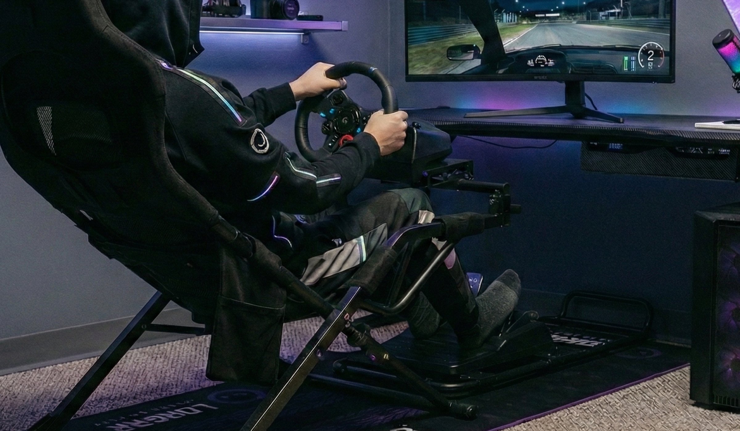 A driver holding a LORGAR cockpit wheel during a race on the monitor, with a LORGAR Sim Racing mat on the floor
